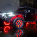 A three quarters view of a black Jeep parked in a puddle, with multiple ORACLE Lighting products installed. All of the LED lighting is turned on and shining brightly, including rock lights, wheel rings, and Vector Grill.