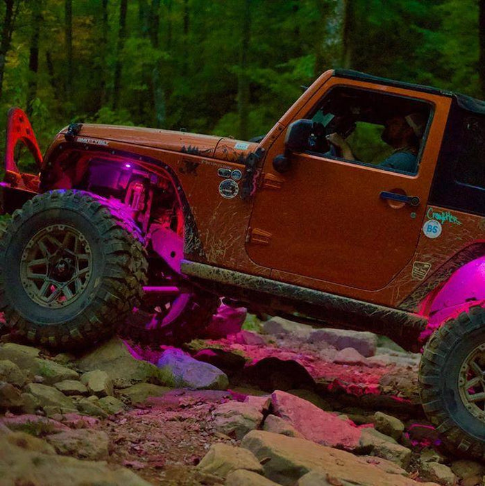 a Jeep driving on a rocky trail, with pink rock lights illuminating the trail.