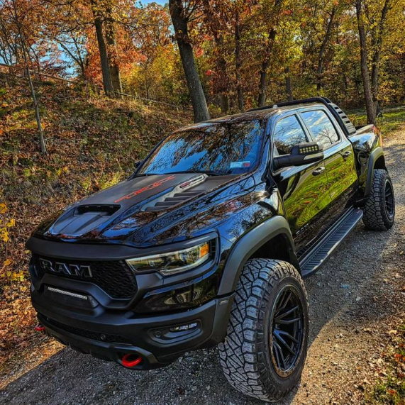 A black RAM TRX driving on a trail outdoors, with multiple ORACLE Lighting products installed, including LED Off-Road Side Mirror Ditch Lights, and Front Bumper Integrated Light Bar.