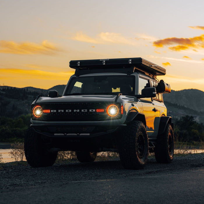 White Ford Bronco riding on a sunset trail, with amber Oculus Headlights turned on.