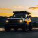 White Ford Bronco riding on a sunset trail, with amber Oculus Headlights turned on.