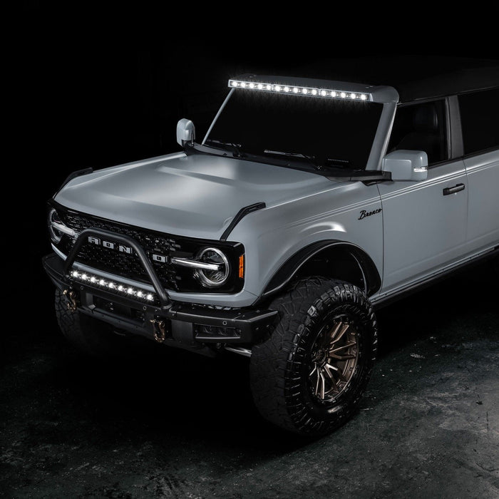 Three quarters view of a grey Ford Bronco with multiple ORACLE Lighting products installed, including the Integrated Windshield Roof LED Light Bar System.